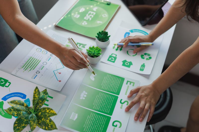 Two adults are reviewing the ESG principles at a table indoors with themes of environment, social, and governance printed on them.