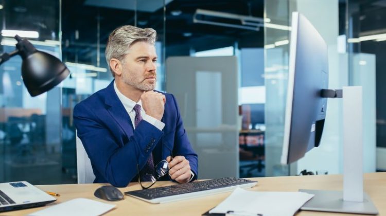 Pensive boss working at computer in modern office, successful male businessman