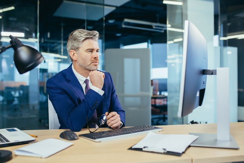 Pensive boss working at computer in modern office, successful male businessman