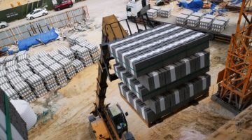 Excavator transporting stacked concrete blocks at a busy construction site.
