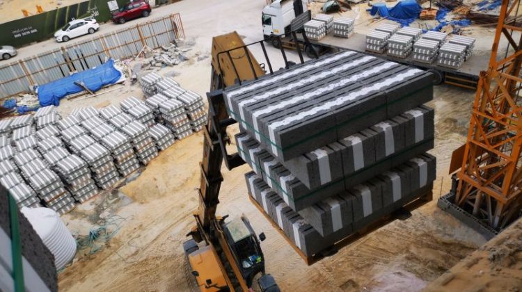 Excavator transporting stacked concrete blocks at a busy construction site.
