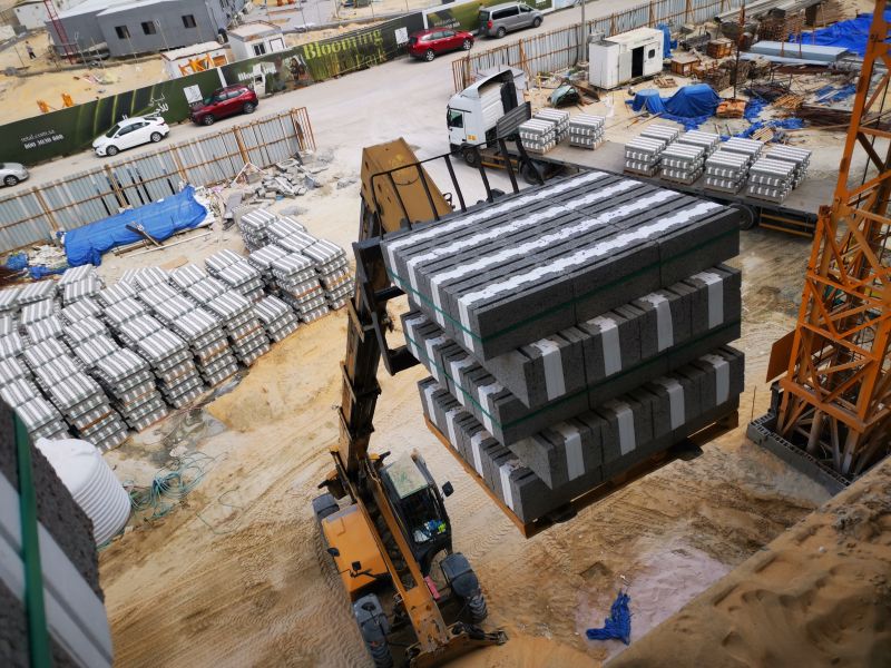 Excavator transporting stacked concrete blocks at a busy construction site.