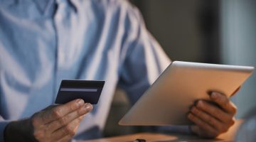 Business owner holding a payment card and tablet while reviewing an online loan application.
