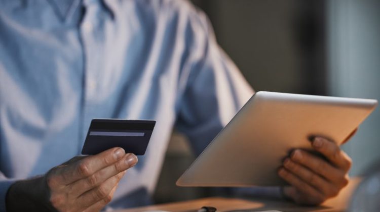 Business owner holding a payment card and tablet while reviewing an online loan application.