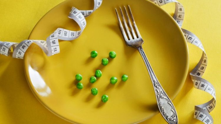 Yellow plate with a fork, a few peas and a measuring tape representing restrictive weight-loss approaches.