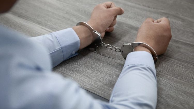 Handcuffed person seated at a table after being charged with a crime.